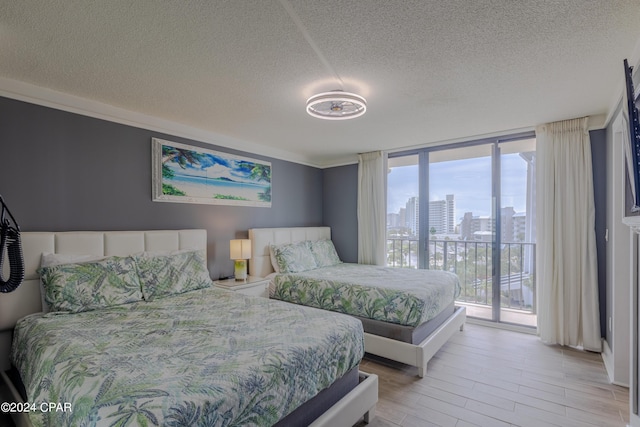 bedroom featuring access to exterior, a city view, light wood finished floors, a textured ceiling, and a wall of windows