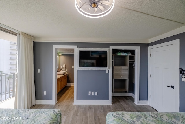 unfurnished bedroom with a textured ceiling, multiple windows, wood finished floors, and a walk in closet