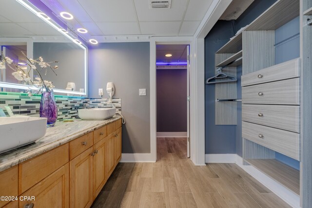 bathroom featuring vanity, a paneled ceiling, wood-type flooring, and tasteful backsplash