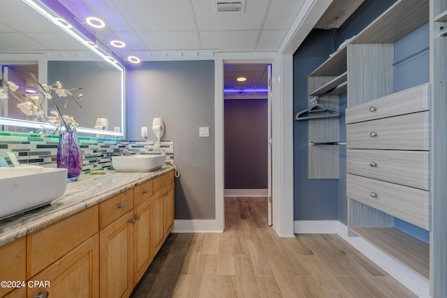 full bath featuring a drop ceiling, wood finished floors, visible vents, backsplash, and double vanity