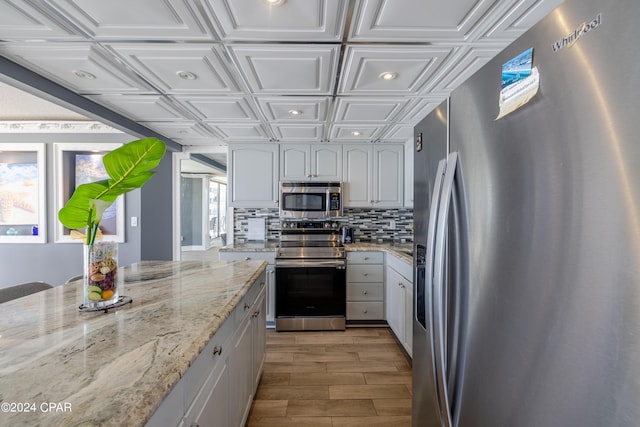 kitchen featuring light stone countertops, light hardwood / wood-style flooring, backsplash, stainless steel appliances, and white cabinetry