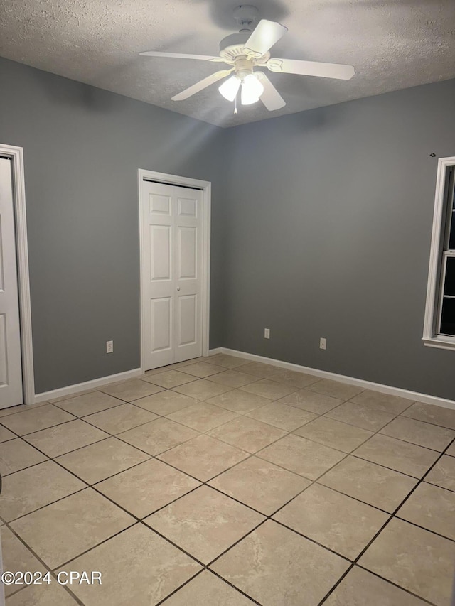 tiled empty room with vaulted ceiling, ceiling fan, and a textured ceiling