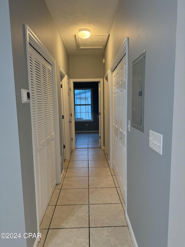 hall featuring a textured ceiling, electric panel, and light tile patterned floors