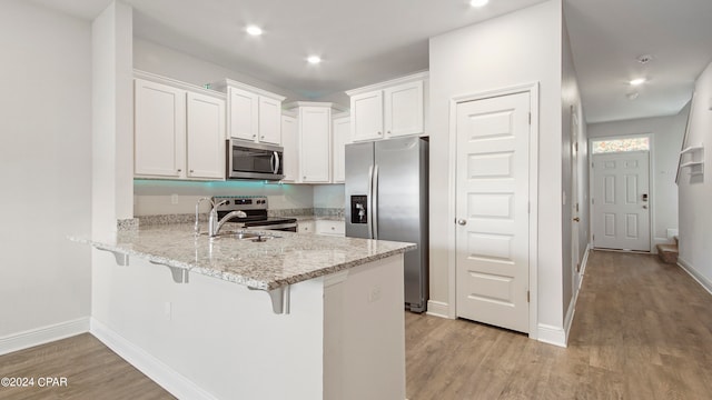 kitchen with kitchen peninsula, light hardwood / wood-style flooring, white cabinetry, appliances with stainless steel finishes, and a breakfast bar area