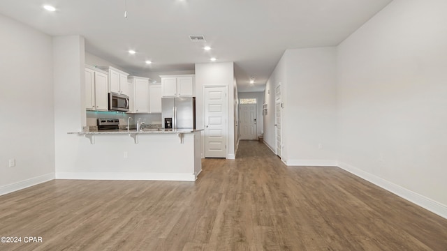 kitchen featuring kitchen peninsula, white cabinetry, appliances with stainless steel finishes, a kitchen breakfast bar, and light wood-type flooring