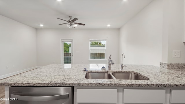 kitchen with stainless steel dishwasher, ceiling fan, light stone counters, and sink