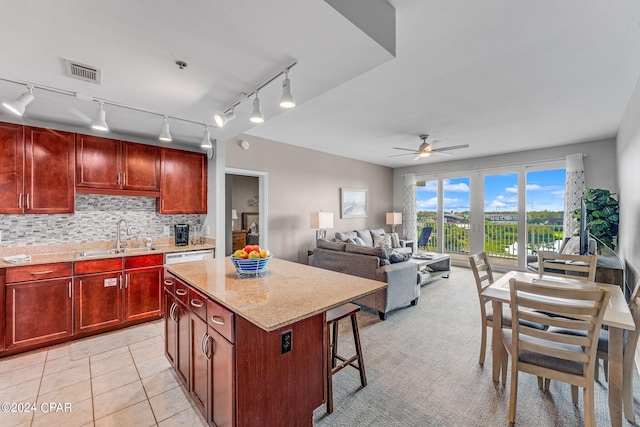 kitchen with tasteful backsplash, light stone counters, sink, ceiling fan, and a center island