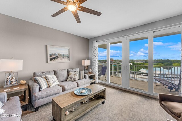 living room featuring ceiling fan, a water view, and light colored carpet