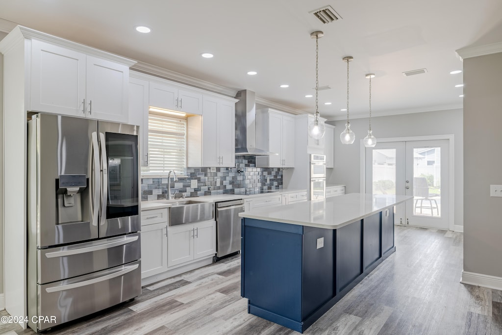 kitchen with white cabinets, appliances with stainless steel finishes, decorative light fixtures, and wall chimney range hood