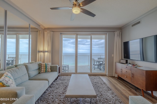 living room with ceiling fan, ornamental molding, a textured ceiling, light hardwood / wood-style floors, and a water view