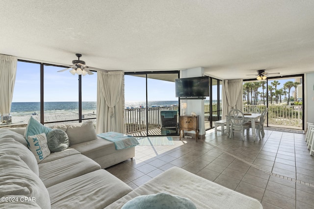 tiled living room featuring expansive windows, ceiling fan, a textured ceiling, and a water view