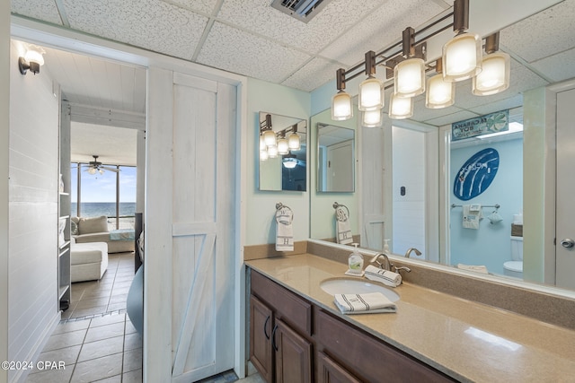 bathroom featuring tile patterned floors, a drop ceiling, vanity, ceiling fan, and toilet