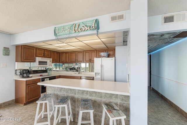 kitchen featuring a breakfast bar area, a paneled ceiling, light tile patterned flooring, and white appliances