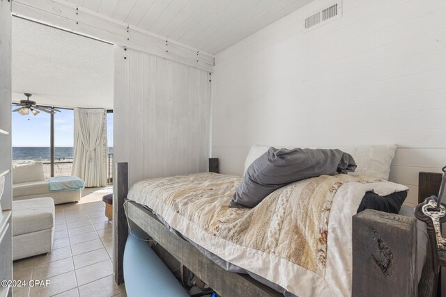 bedroom with wood walls, a water view, and light tile patterned flooring