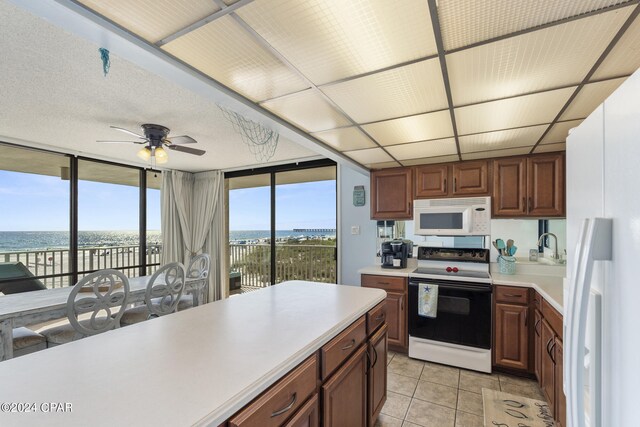 kitchen featuring ceiling fan, expansive windows, white appliances, a water view, and light tile patterned floors