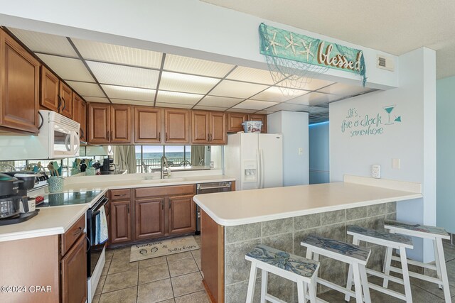 kitchen featuring sink, kitchen peninsula, white appliances, a breakfast bar, and light tile patterned floors