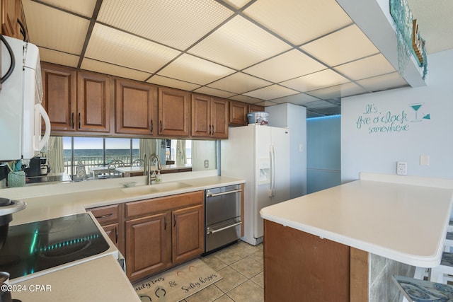 kitchen with white appliances, sink, light tile patterned flooring, a kitchen bar, and kitchen peninsula