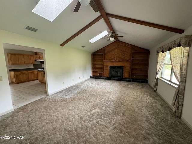 unfurnished living room with ceiling fan, light colored carpet, a tiled fireplace, and lofted ceiling with skylight