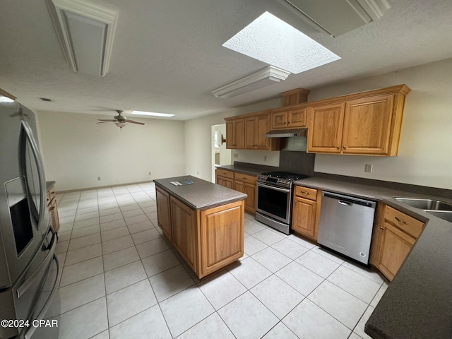 kitchen with appliances with stainless steel finishes, light tile patterned flooring, a kitchen island, ceiling fan, and a skylight