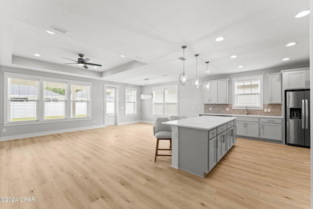 kitchen with decorative light fixtures, tasteful backsplash, gray cabinetry, a center island, and stainless steel fridge with ice dispenser