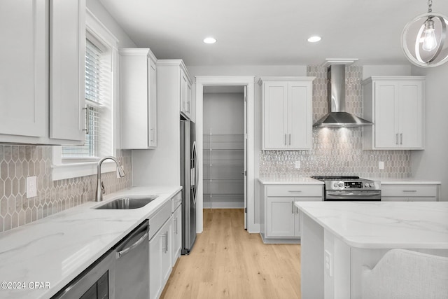 kitchen with sink, appliances with stainless steel finishes, hanging light fixtures, white cabinets, and wall chimney exhaust hood