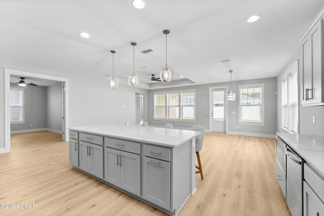 kitchen featuring dishwasher, ceiling fan, gray cabinetry, a center island, and a kitchen bar