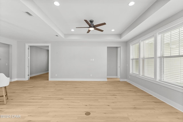 interior space featuring a raised ceiling, ceiling fan, and light wood-type flooring