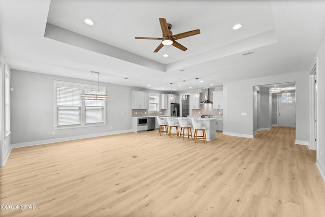 unfurnished living room featuring ceiling fan, a raised ceiling, and light wood-type flooring