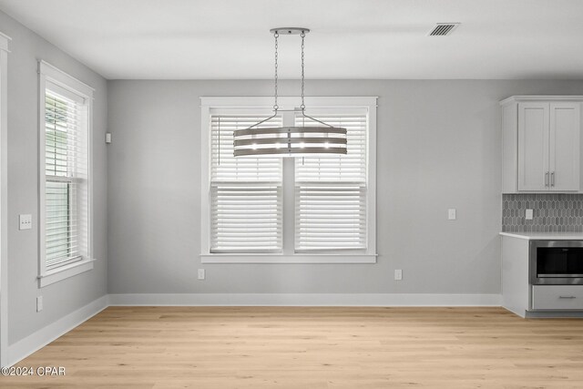 unfurnished dining area with a notable chandelier and light wood-type flooring