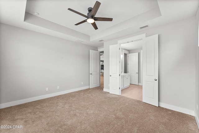 unfurnished bedroom with ceiling fan, a raised ceiling, and light colored carpet