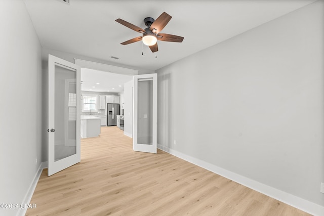 empty room featuring french doors, ceiling fan, and light wood-type flooring