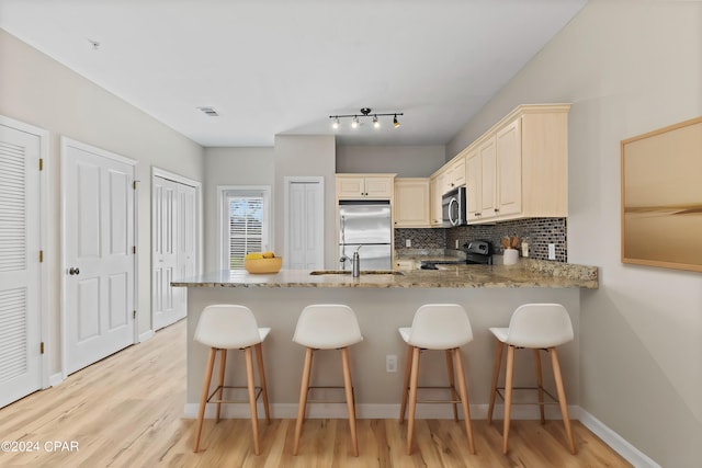 kitchen featuring a breakfast bar, light wood-type flooring, cream cabinetry, stainless steel appliances, and light stone countertops