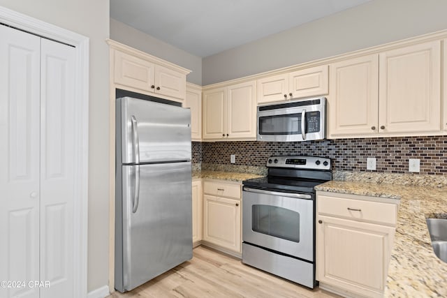 kitchen featuring light hardwood / wood-style floors, backsplash, appliances with stainless steel finishes, light stone countertops, and cream cabinets