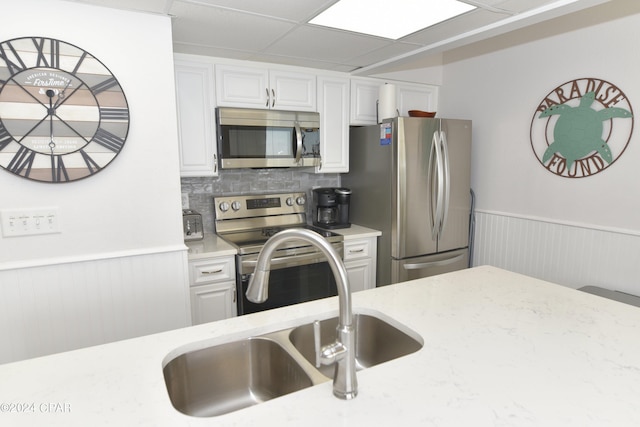 kitchen featuring appliances with stainless steel finishes, white cabinetry, a sink, light stone counters, and wainscoting