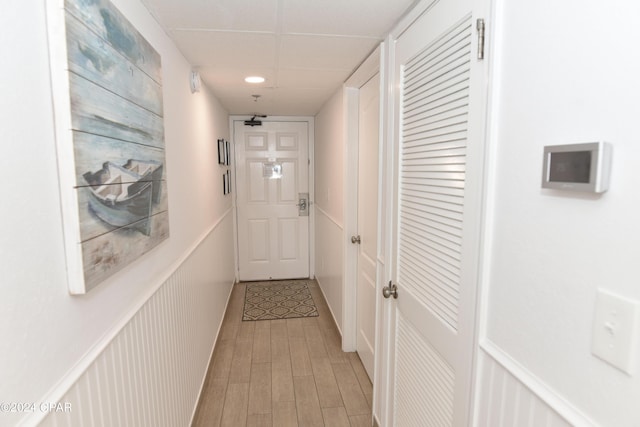 hall featuring light wood finished floors, wainscoting, and a drop ceiling