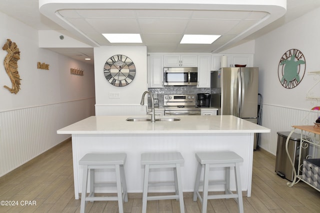 kitchen featuring a wainscoted wall, light wood finished floors, a kitchen bar, appliances with stainless steel finishes, and a sink