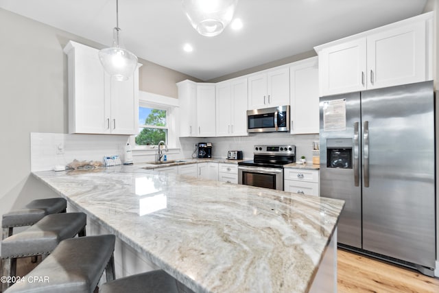 kitchen with appliances with stainless steel finishes, white cabinetry, kitchen peninsula, decorative light fixtures, and sink