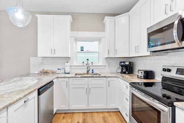 kitchen featuring light hardwood / wood-style floors, white cabinetry, stainless steel appliances, decorative light fixtures, and sink