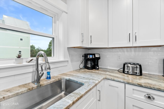 kitchen with tasteful backsplash, sink, light stone counters, and white cabinets