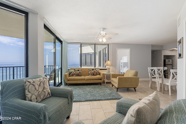 tiled living room with ceiling fan, a textured ceiling, floor to ceiling windows, and a water view