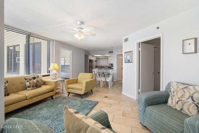 living room featuring ceiling fan, light tile patterned floors, and a textured ceiling