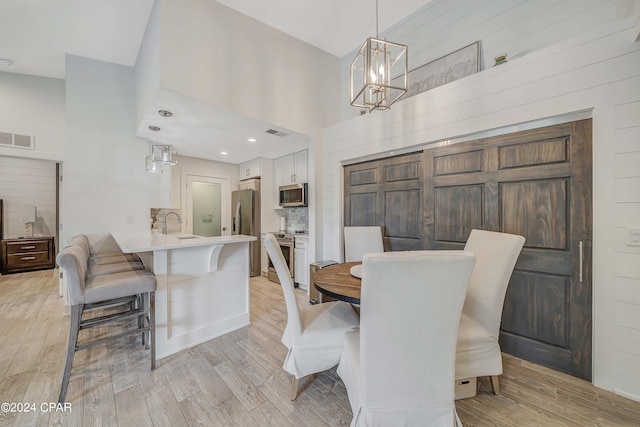 dining area with light wood-type flooring, a high ceiling, sink, and a notable chandelier