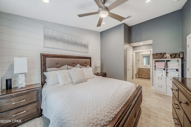 bedroom with vaulted ceiling, wood walls, ceiling fan, light hardwood / wood-style flooring, and ensuite bathroom