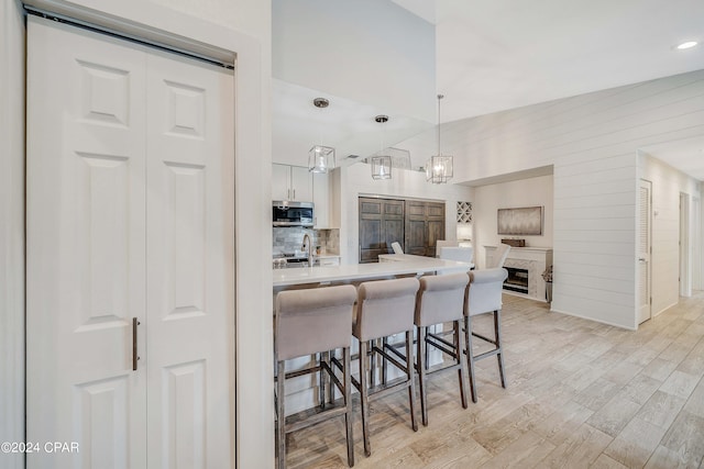 kitchen with light wood-type flooring, a breakfast bar area, white cabinets, lofted ceiling, and decorative light fixtures