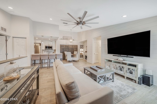 living room featuring ceiling fan with notable chandelier, light hardwood / wood-style flooring, and a high ceiling