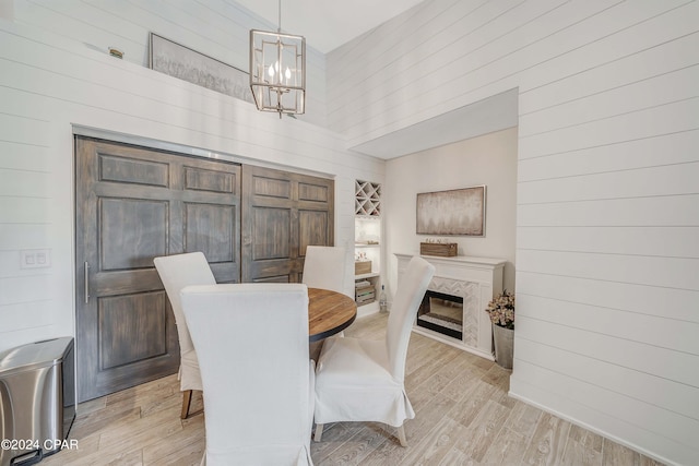 dining space featuring light hardwood / wood-style floors, a towering ceiling, a fireplace, an inviting chandelier, and wooden walls