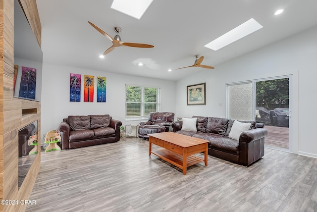 living room featuring ceiling fan, lofted ceiling with skylight, a fireplace, and light hardwood / wood-style flooring