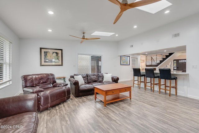 living room featuring ceiling fan, light hardwood / wood-style flooring, and a skylight