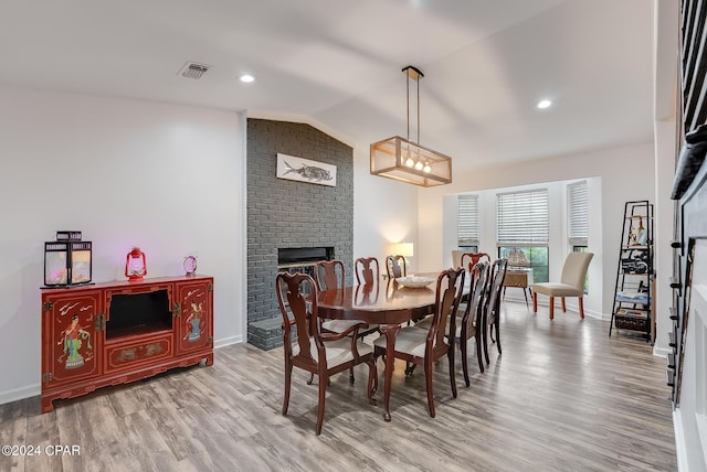 dining space featuring a brick fireplace, light wood-type flooring, and vaulted ceiling