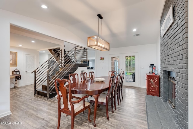 dining space with hardwood / wood-style flooring, vaulted ceiling, french doors, and a brick fireplace